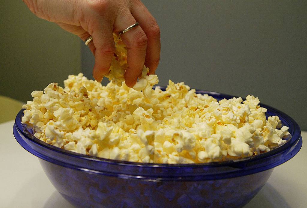 A woman grabs freshly popped microwave popcorn from a bowl