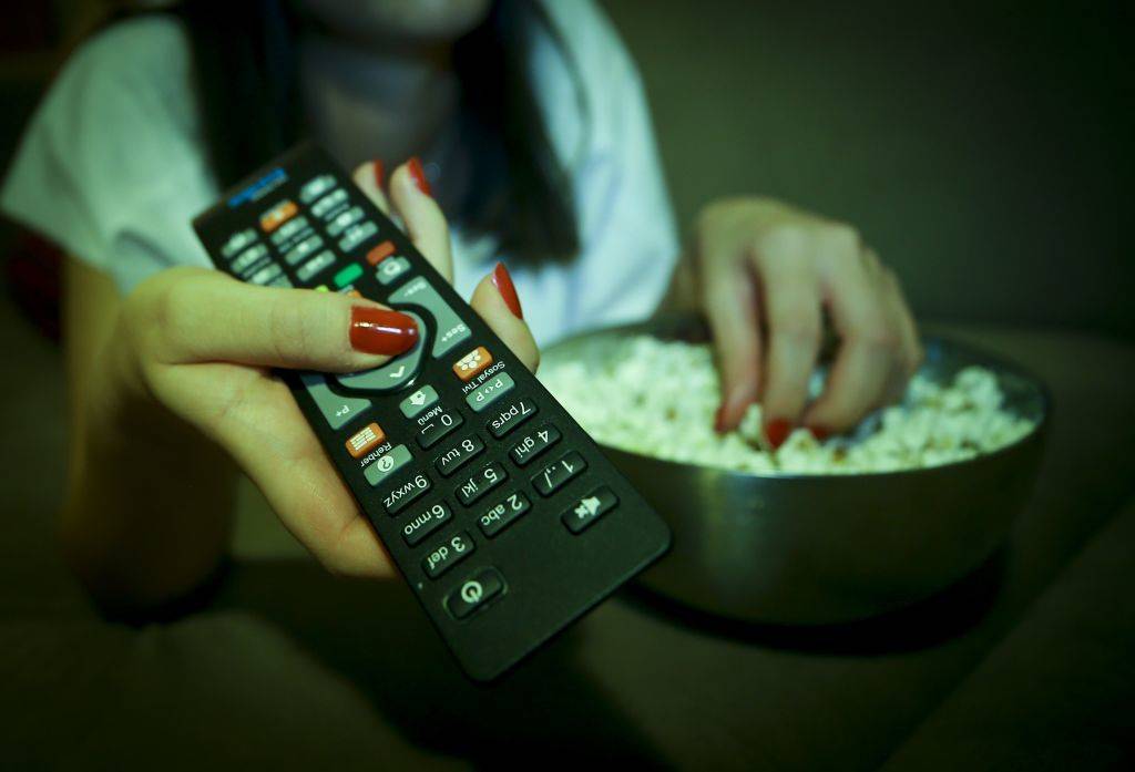 A woman holds a remote controller while eating popcorn