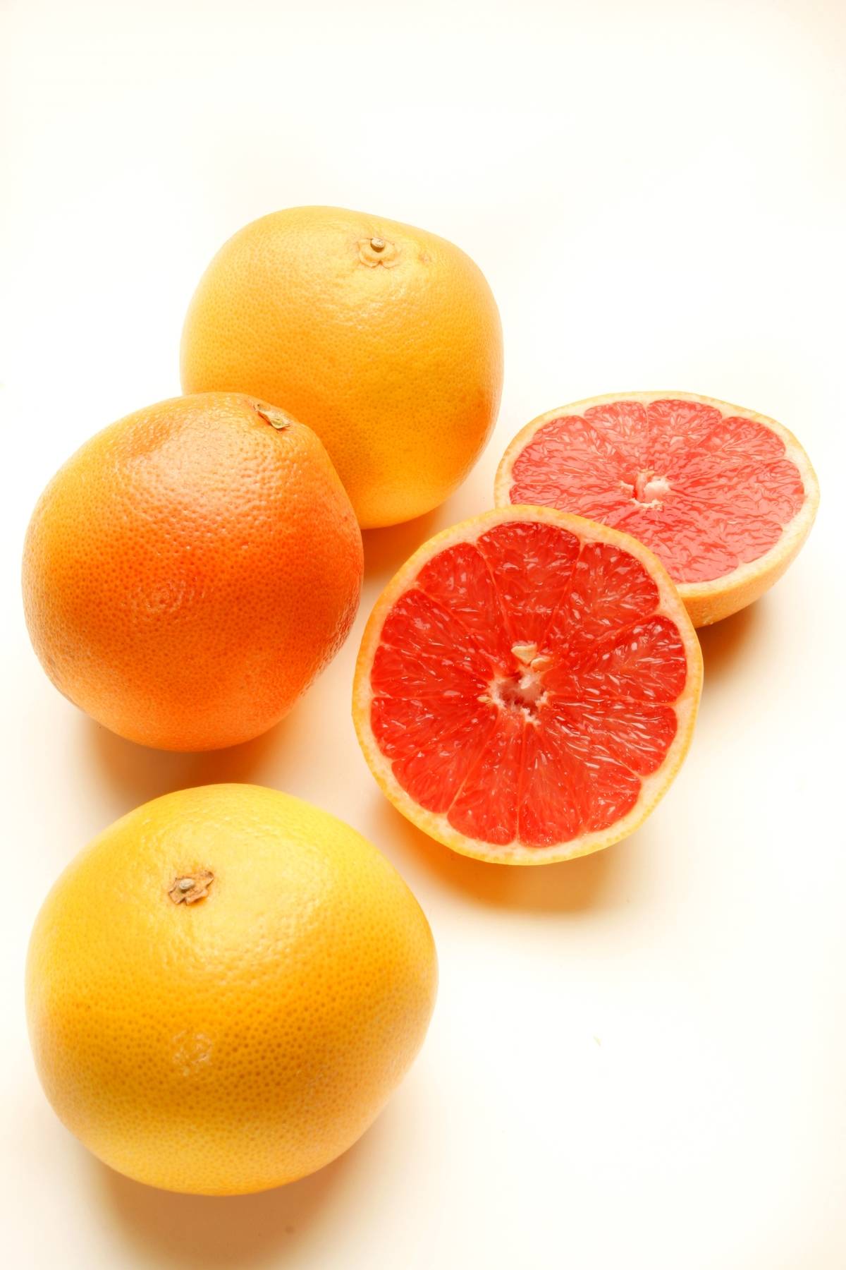 Grapefruits and grapefruit slices lay against a white background.