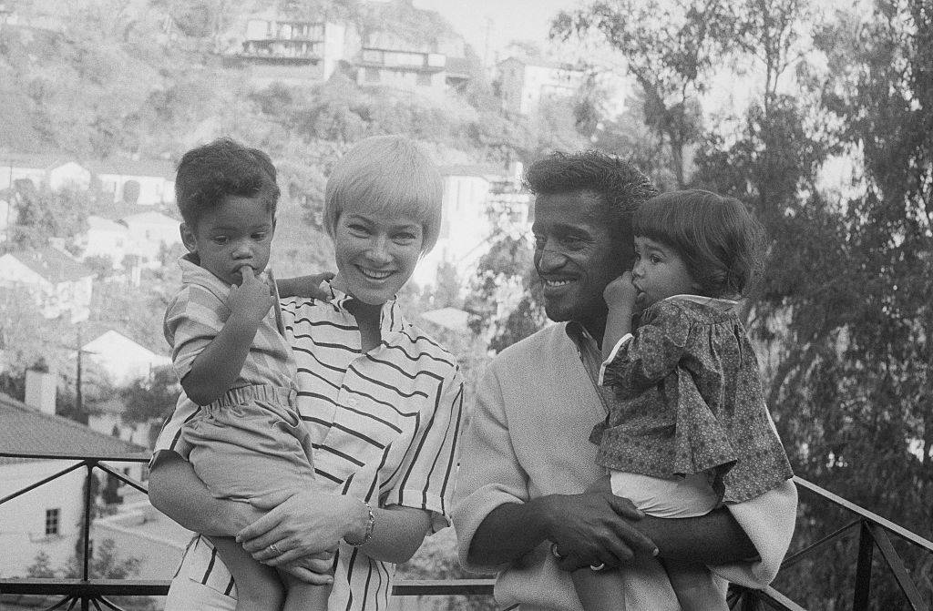 Versatile entertainer Sammy Davis, Jr., and his wife, actress May Britt, pose with their newly enlarged family in the garden of their home November 10th