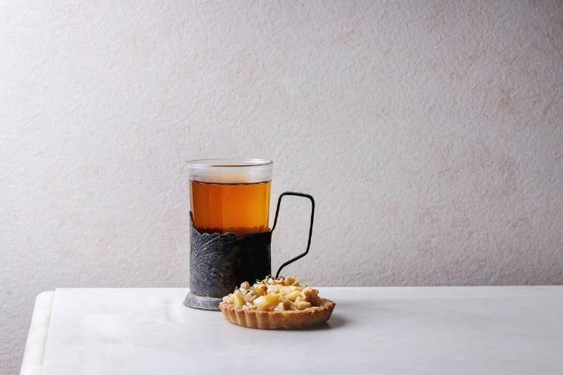 homemade-sweet-apple-shortbread-tartlet-in-white-plate.-glass-of-hot-tea-in-vintage-cup-holder-on-white-marble-table.-autumn-baking.-minimalist-style.-47651