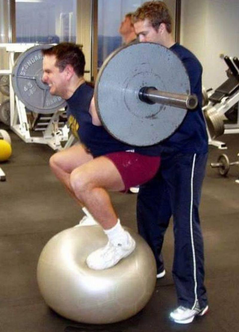Man standing on yoga ball while lifting weights