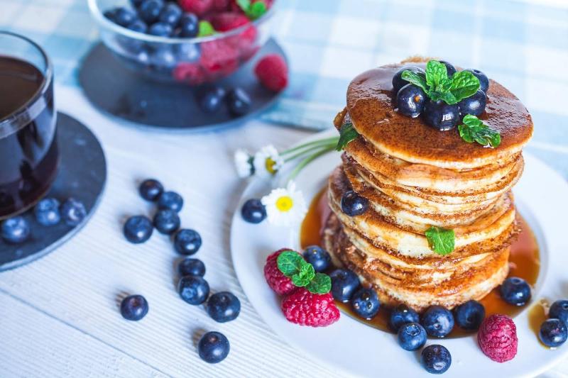 A large stack of blueberry pancakes is surrounded by blueberries.