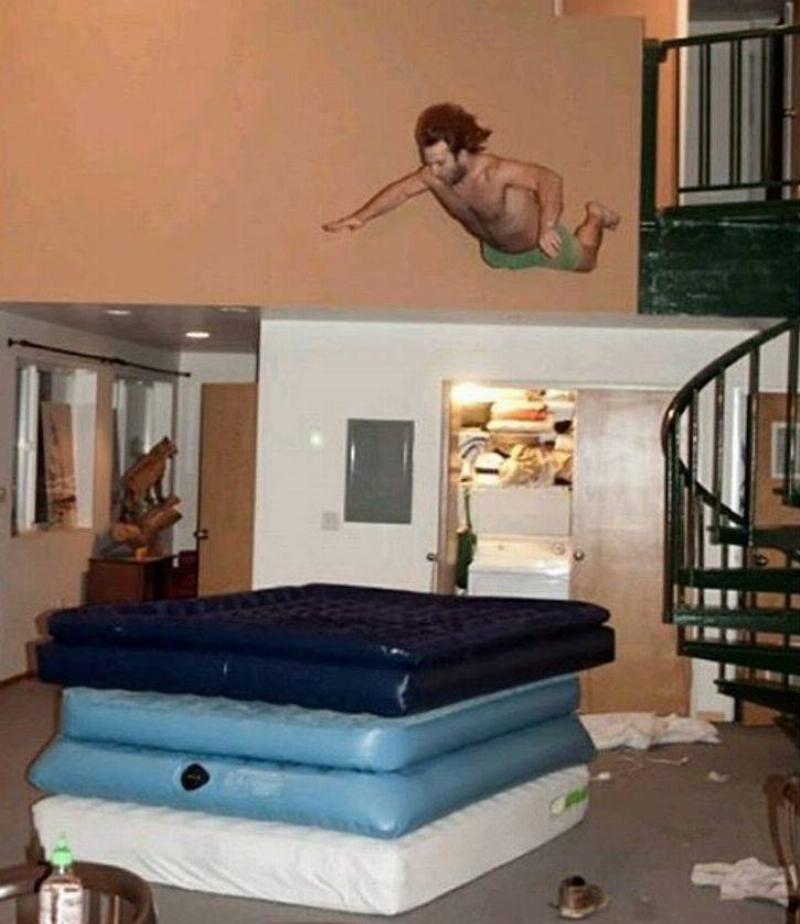 person jumping from balcony onto pile of inflatable mattresses