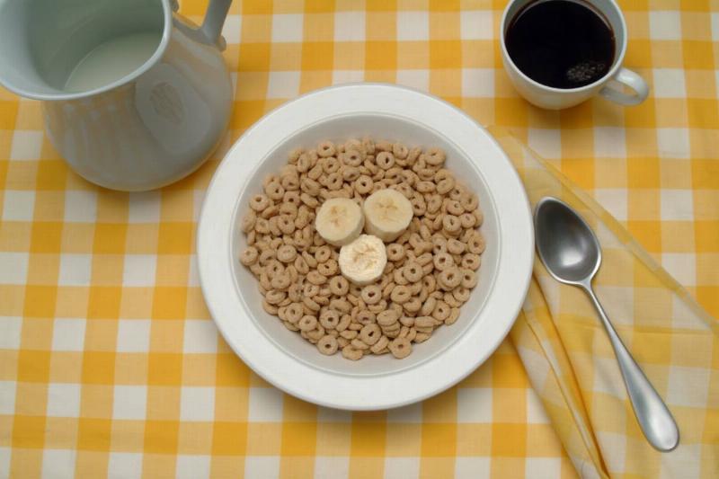 A woman reads a magazine while eating cereal.