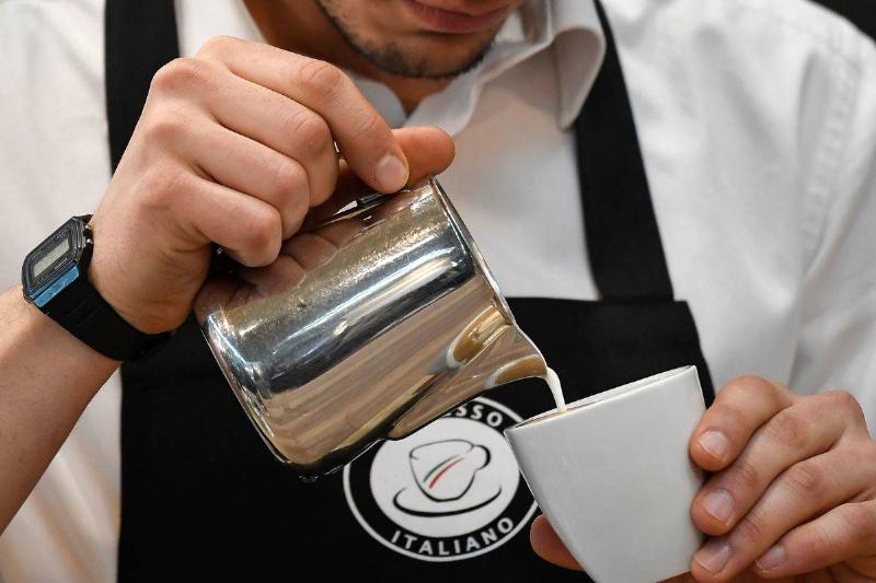 A barista pours cream into a coffee.