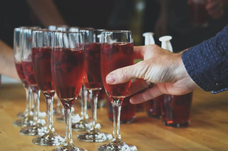 A person picks up a glass of cranberry juice from a serving tray.