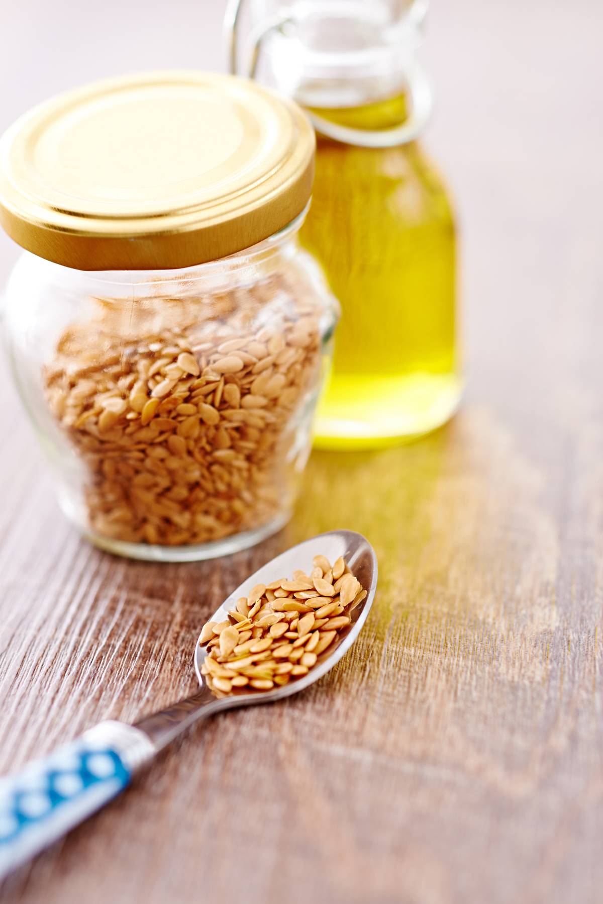 A spoon full of flax seeds sits next to a jar of seeds.