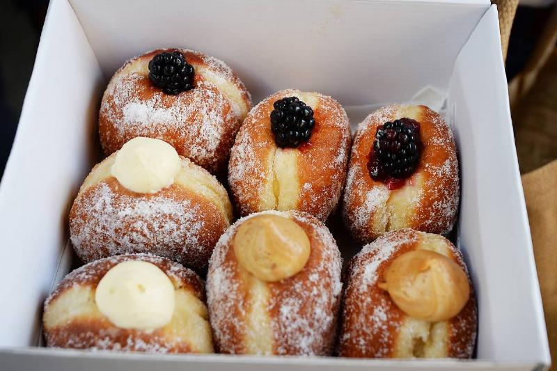 Jelly-filled donuts in a box are topped with berries and cream.