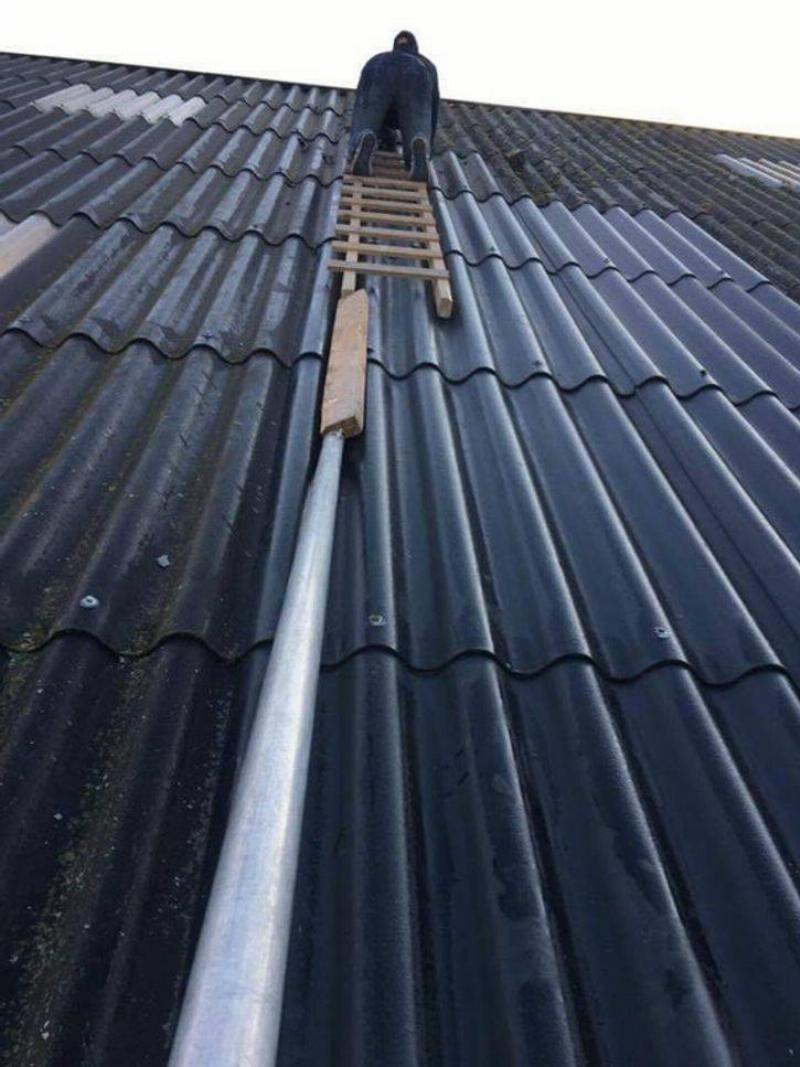 person on roof with ladder balanced on boards and pipes