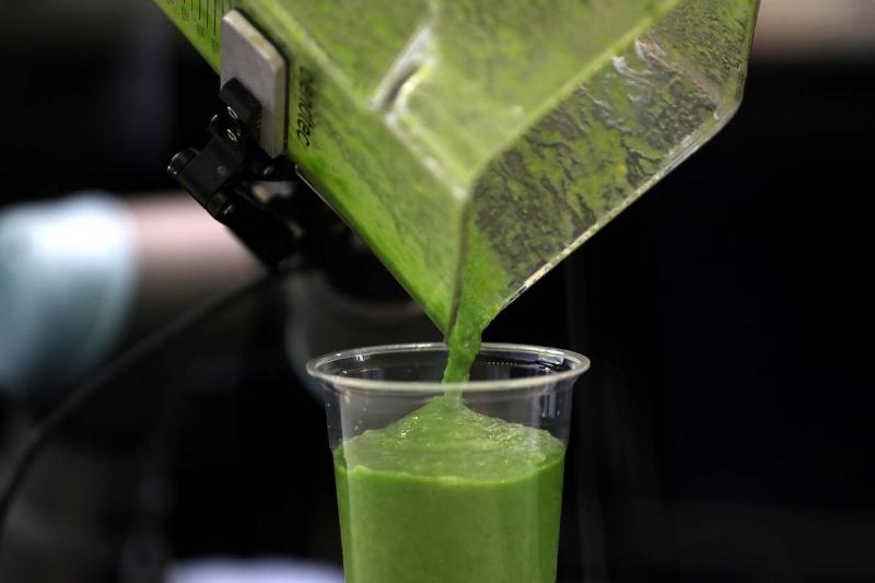 A person pours a green smoothie into a glass.