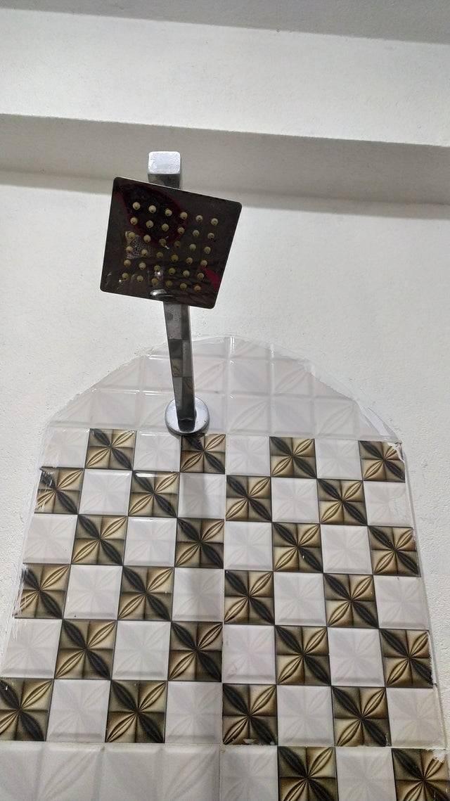 Crooked showerhead with golden & white checker tiles underneath 
