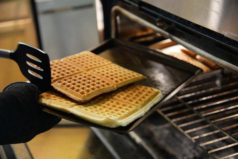 A chef takes Belgian waffles out of an oven.