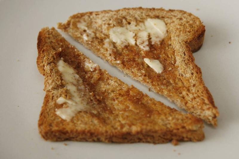 A piece of plain, whole grain toast sits on a black plate.