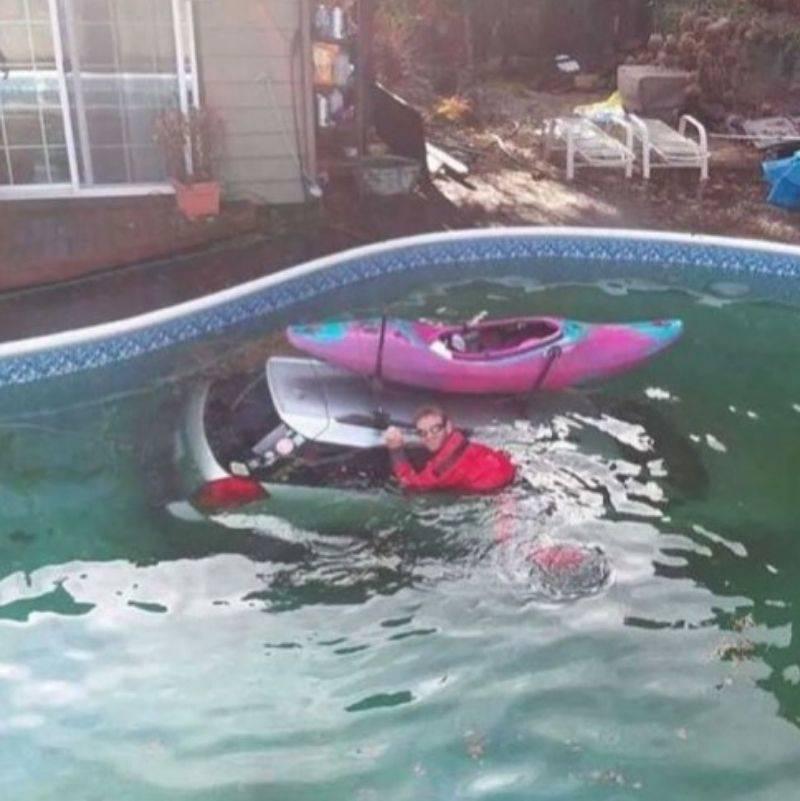 a guy in the pool holding onto his car that sunk with a boat on top