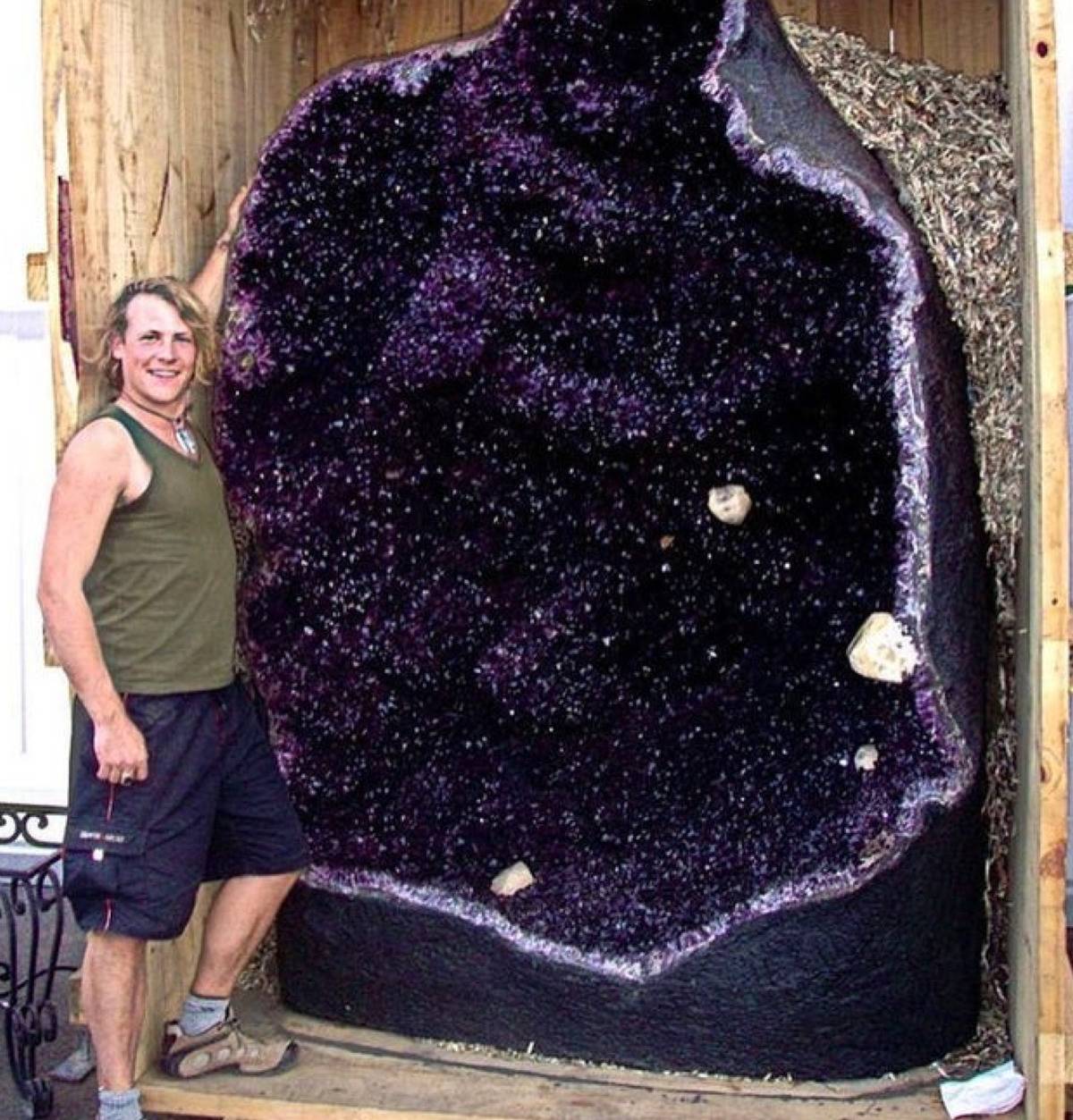 guy standing next to a huge amethyst that is bigger than he is 