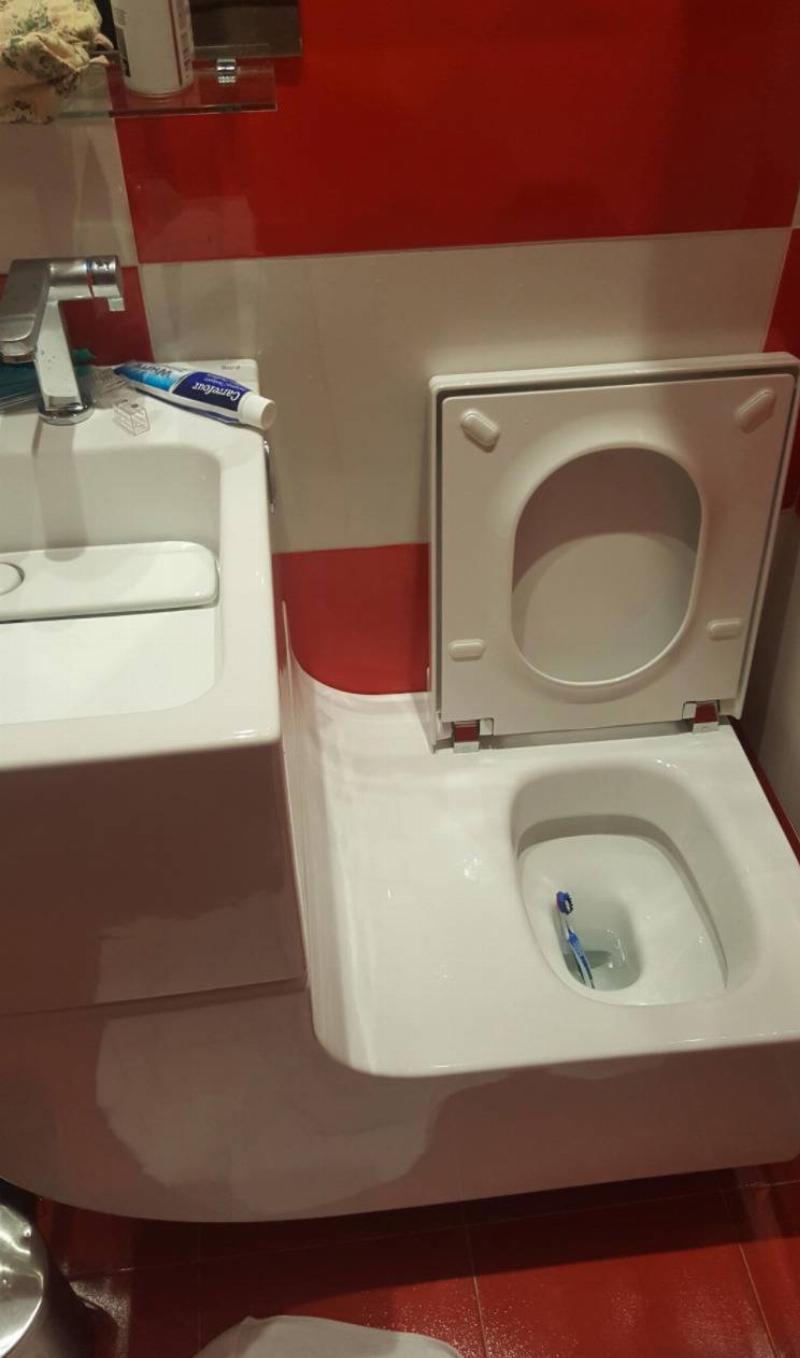 sink counter has slope attaching it to toilet with toothbrush inside the toilet