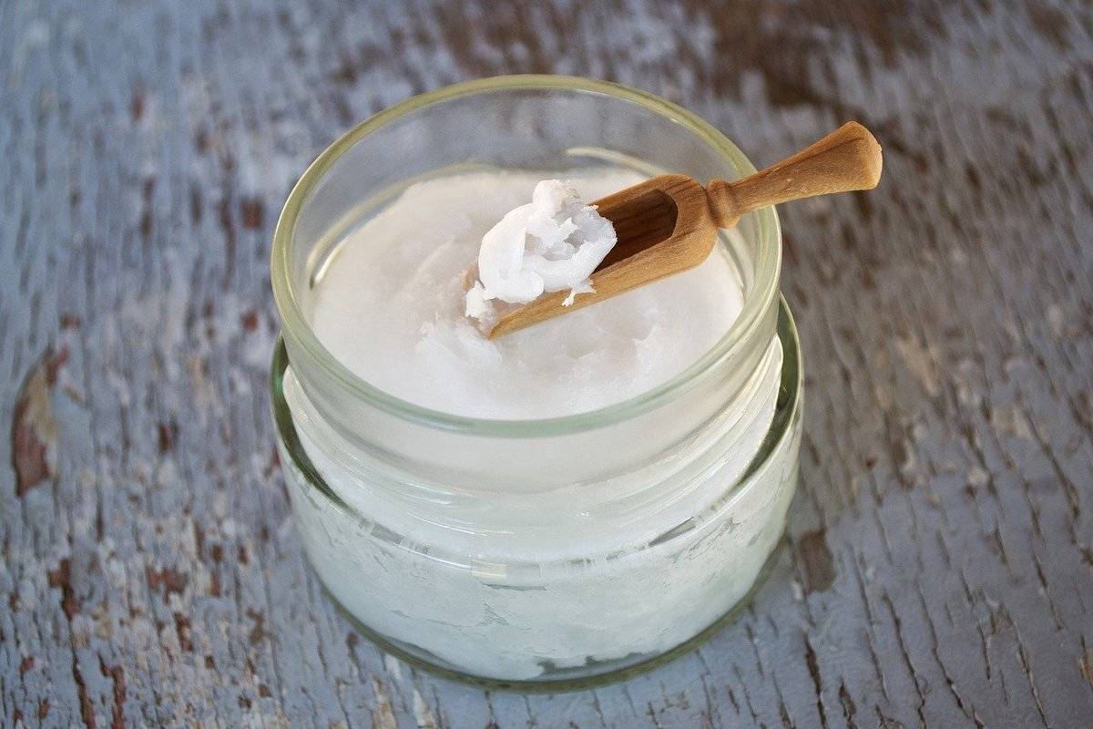 Coconut oil is contained in a glass jar with a small wooden spoon.
