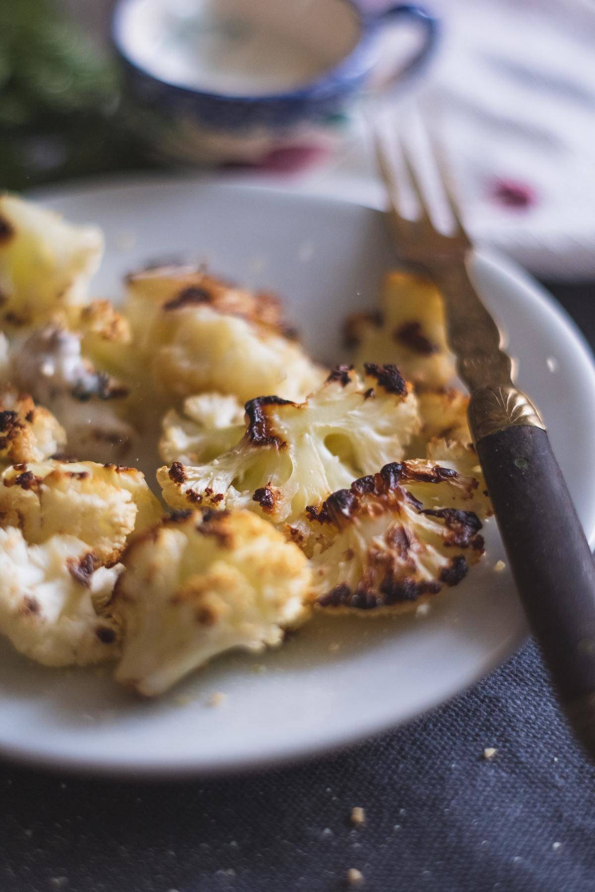 Cooked and charred cauliflower is on a white plate with a fork.