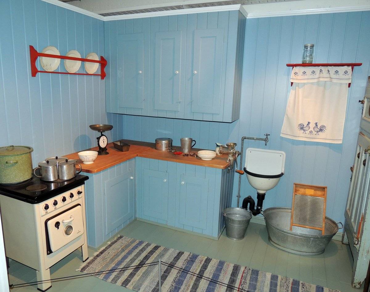 A blue kitchen from 1945 features wooden countertops, plates on display, and embroidered curtains.
