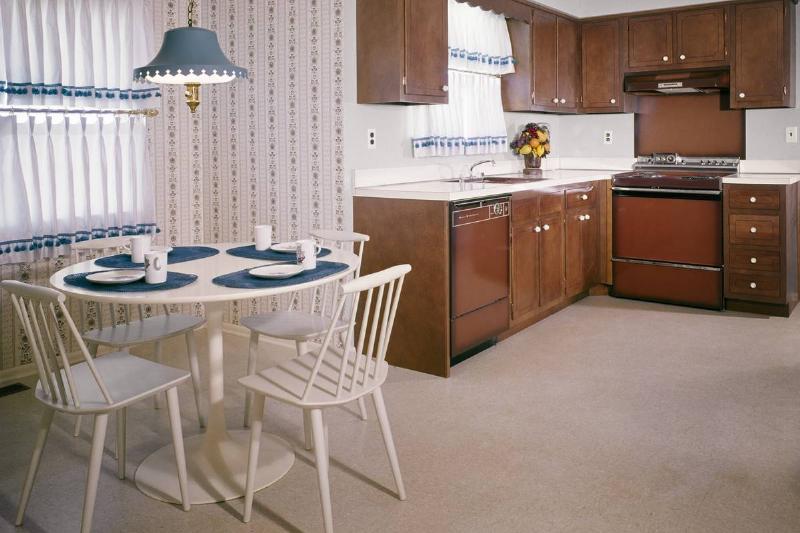 In a 1960s dining room/kitchen area, the wall is decorated with patterned wallpaper.