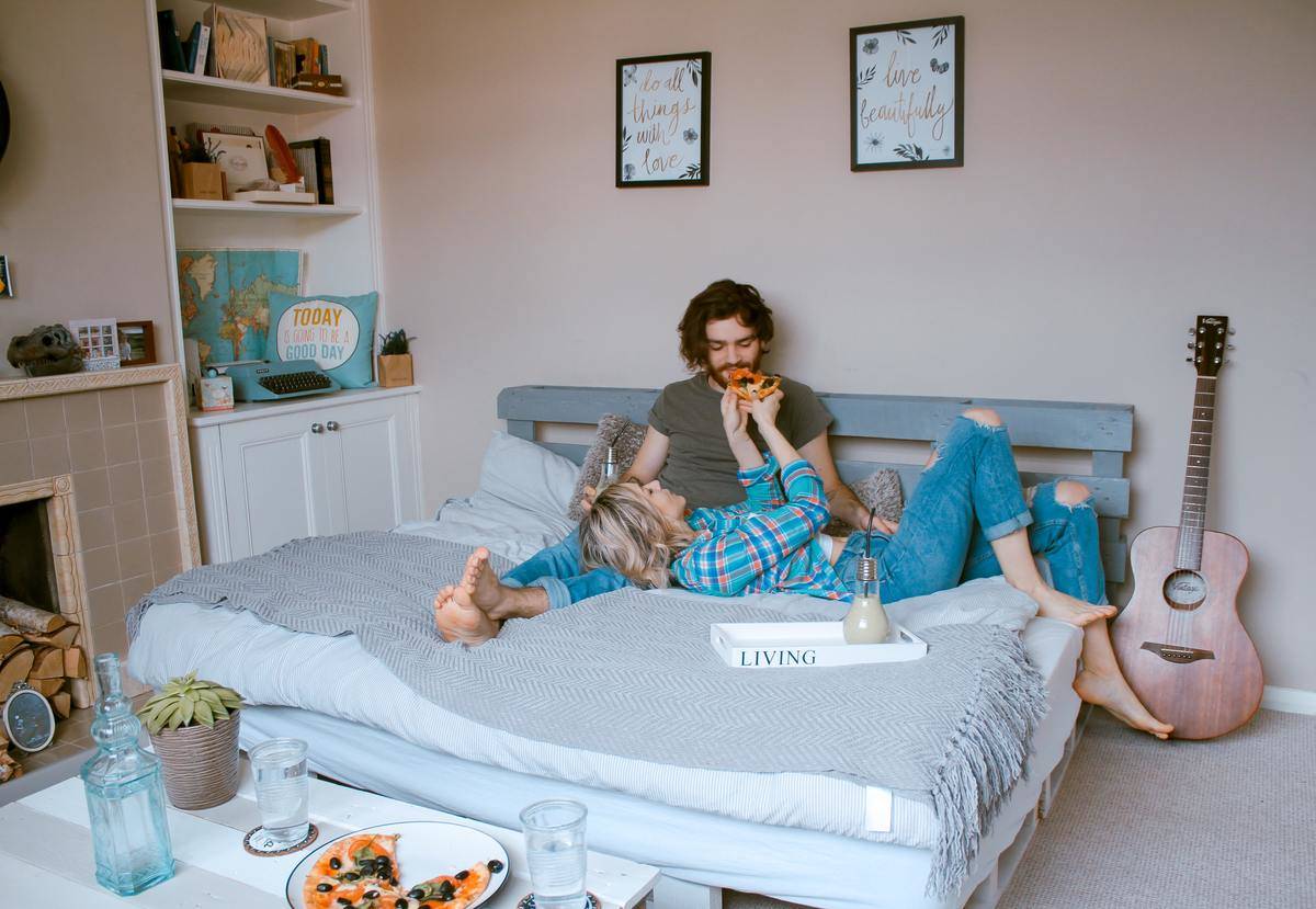 woman feeding pizza to man in bed