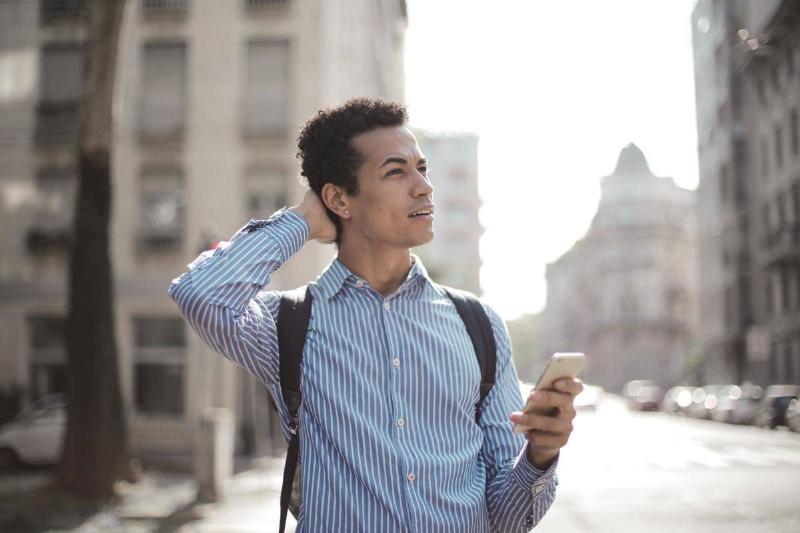 Man outside holding cell phone looking up confused