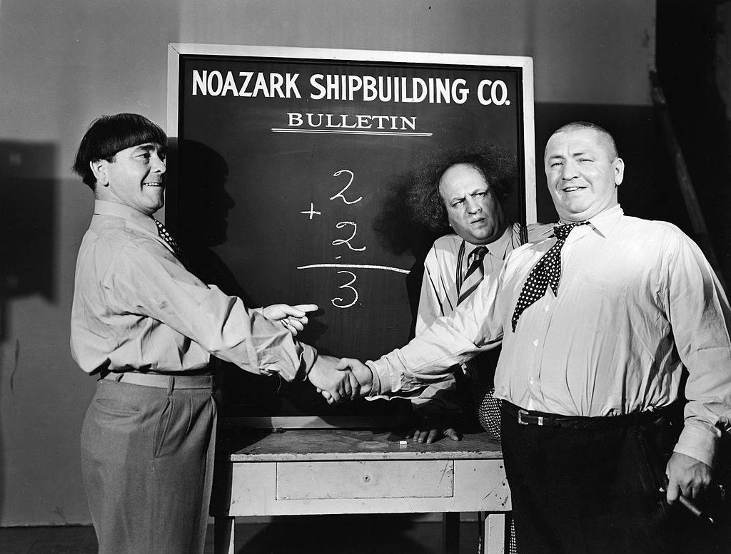 Curly and Moe Stooges shake hands in front of Nozark Ship building sign 