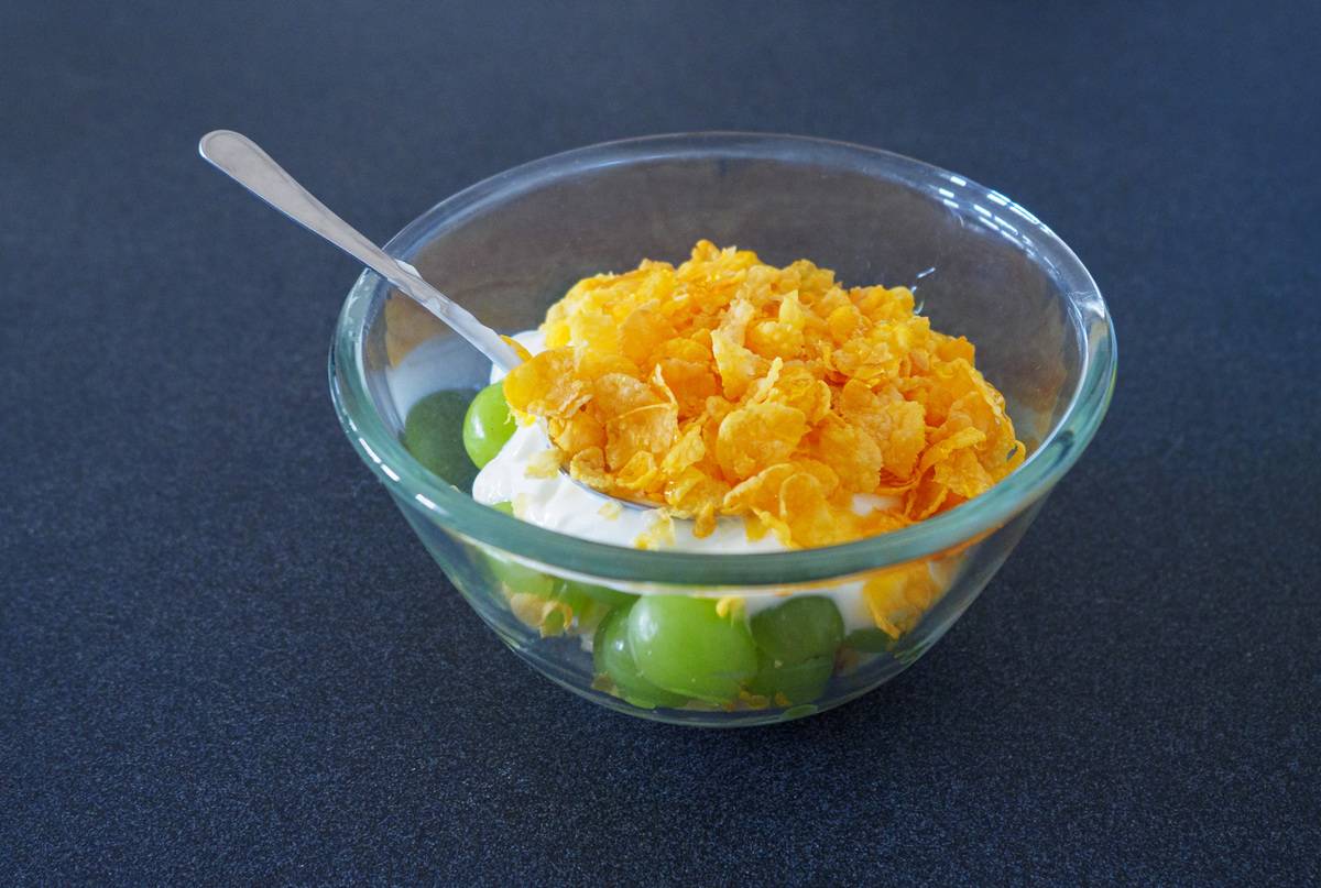 A glass bowl of sugar-free cereal, yogurt and grapes on a table.