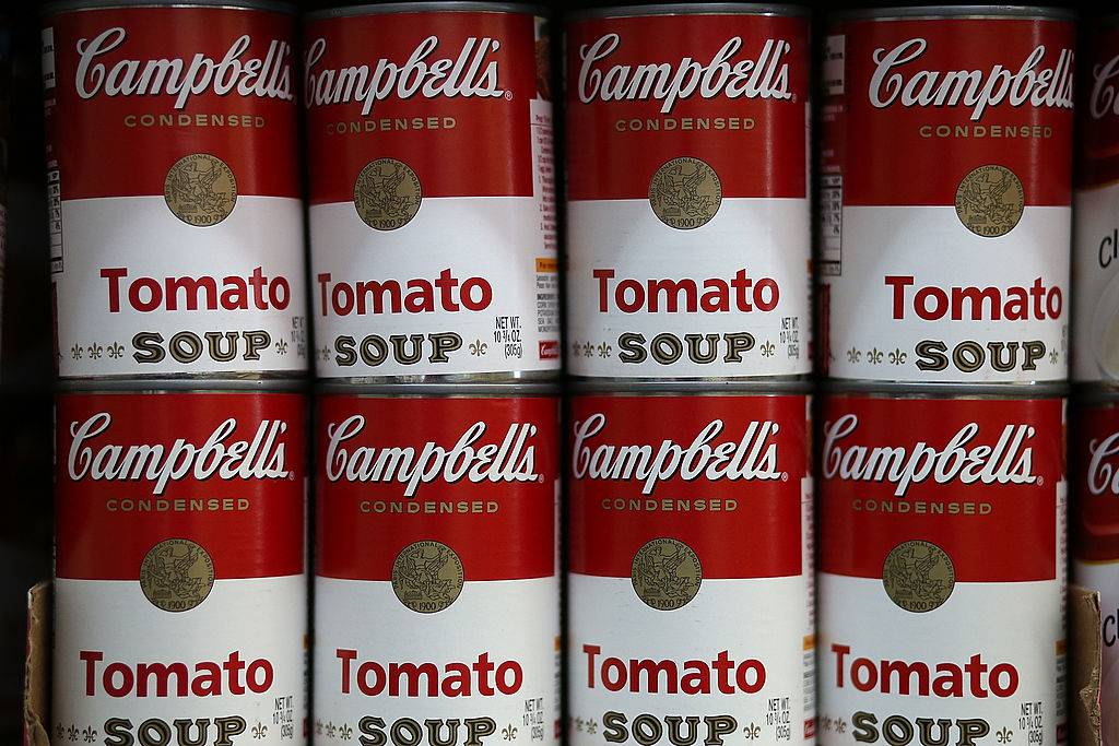 Cans of Campbell's tomato soup are displayed on a shelf