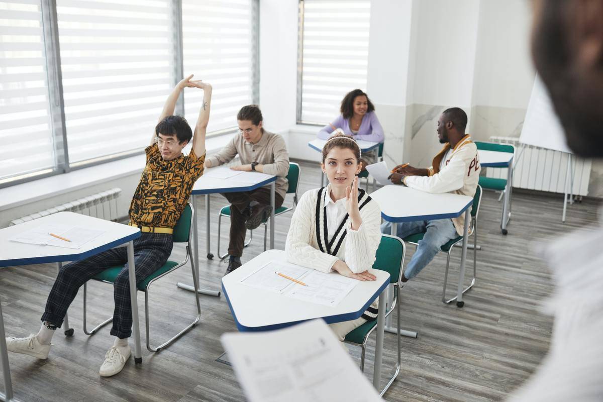 Kids in classroom, one boy leans back stretching in his desk