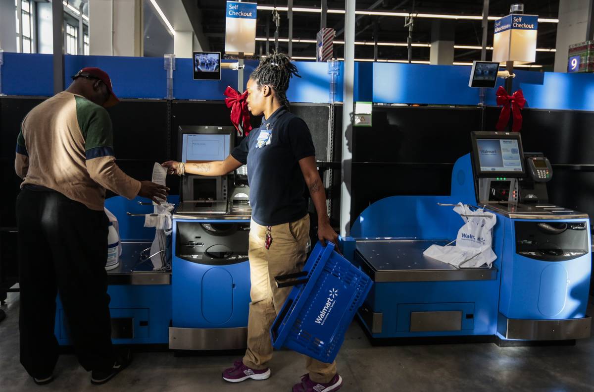 Woman working at Walmart monitors self-checkout kiosk 