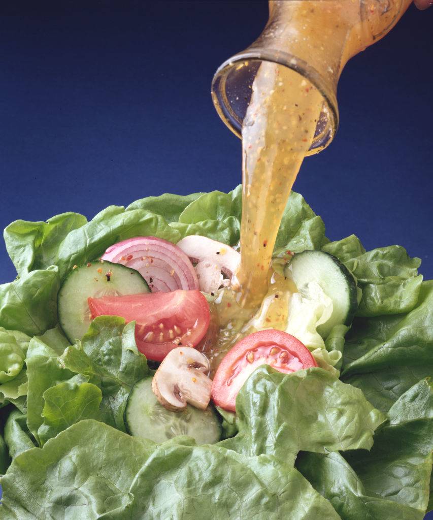 Close-up view of salad dressing getting poured onto a salad