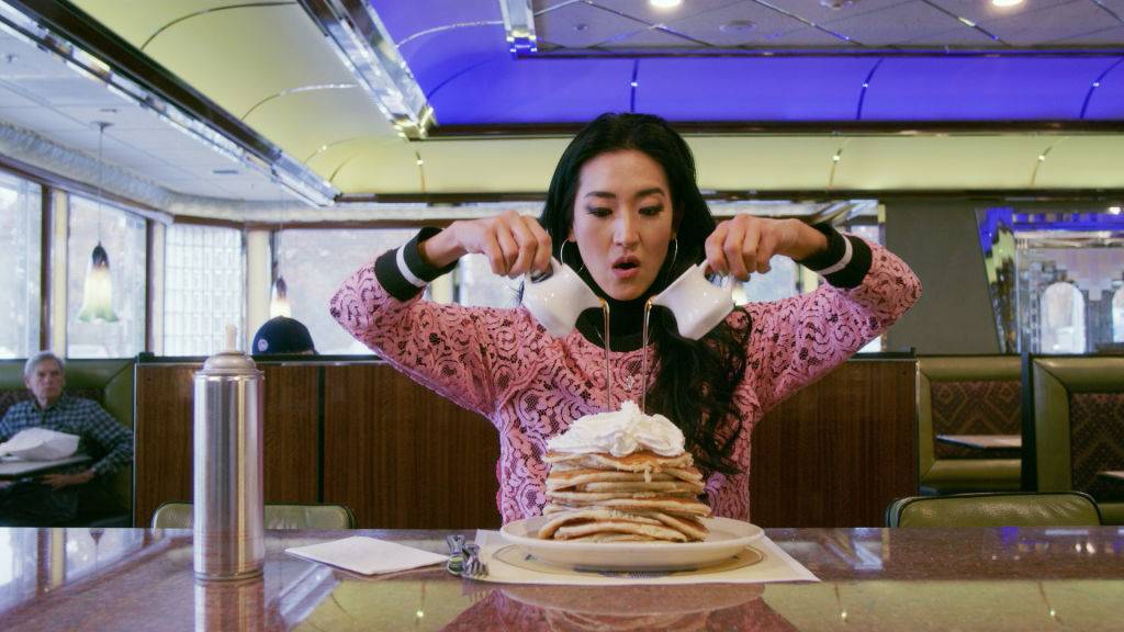 woman pouring syrup onto a stack of pancakes
