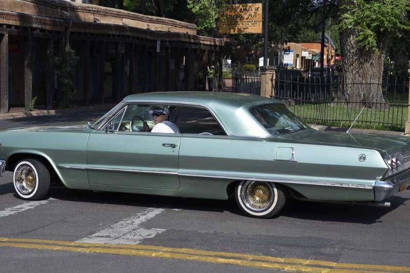 Man driving a blueish-silver 1960s car