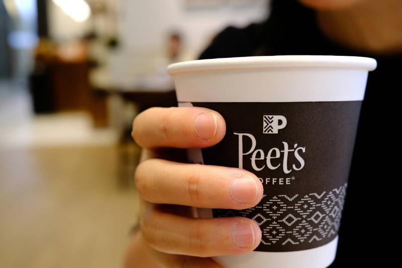 A woman is holding a cup of Peet's coffee in a Peet's Coffee...