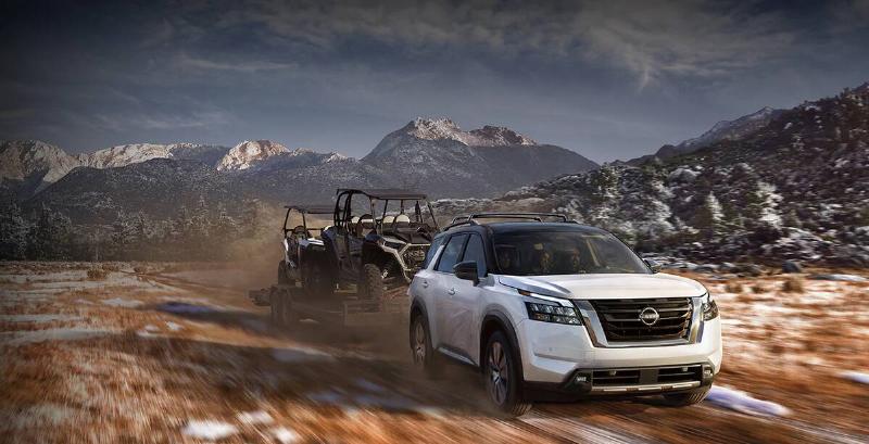 2024-nissan-pathfinder-front-view-driving-off-road-while-towing-flatbed-two-carts