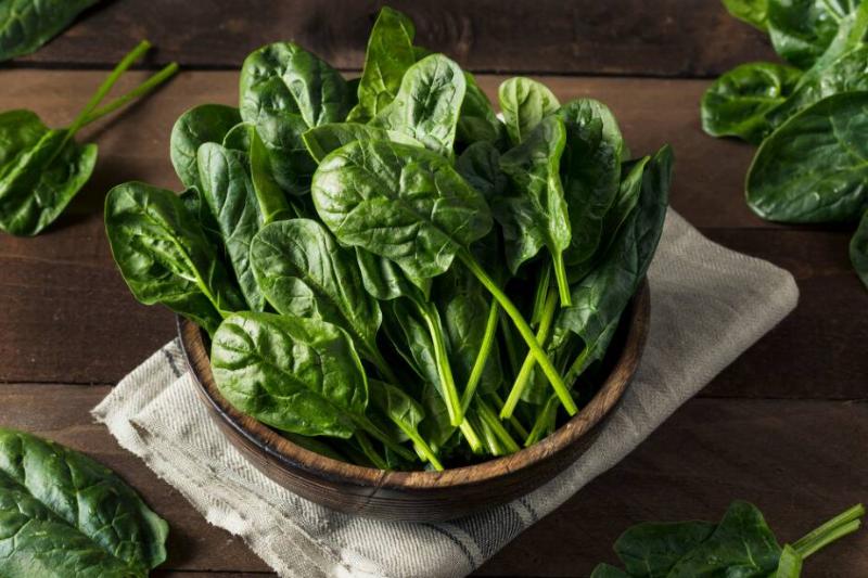 Spinach in a wooden bowl that's been placed atop a tea-towel