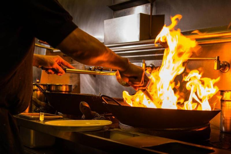 Person off-screen frying food in a pan that has fire emanating off of it