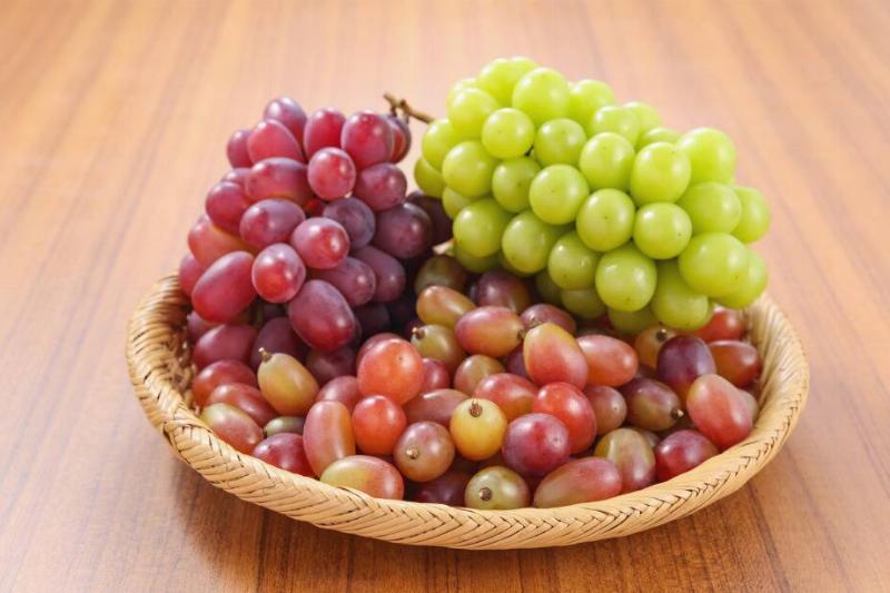 Red and green grapes in a wicker basket that's atop a wooden table