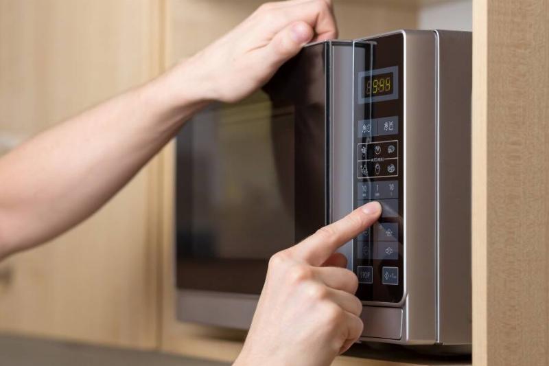Person off-screen pressing buttons on a microwave