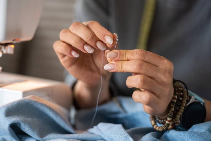 Woman sewing a shirt with a needle. A sewing machine is to the side of the scene