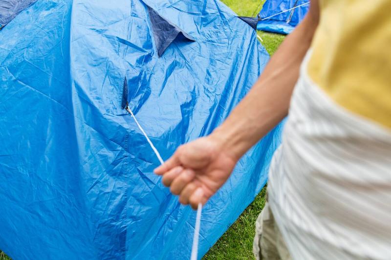 Person pulling a string from a tarp over a tend