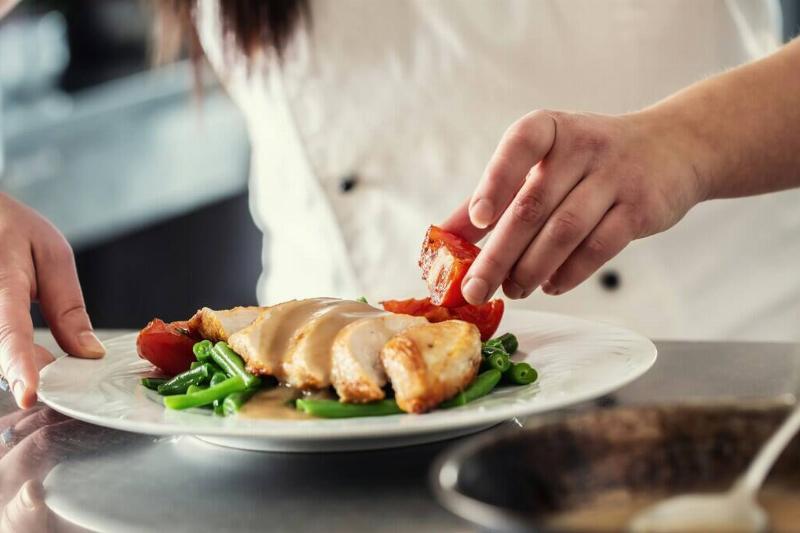 Chef putting together a dish consisting of chicken breast, green beans and tomatoes