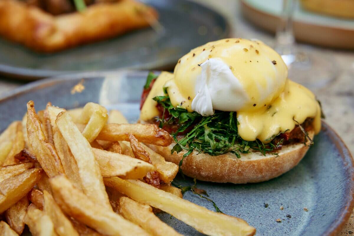 Eggs Benedict atop a bagel, next to fries on a plate