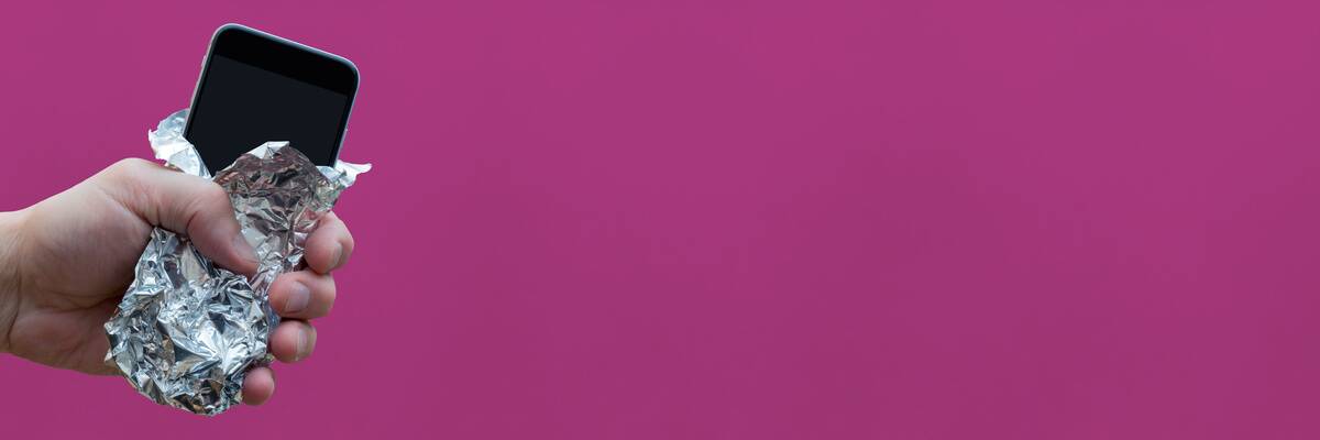 Person off-screen holding out a cellphone partially wrapped in aluminum foil