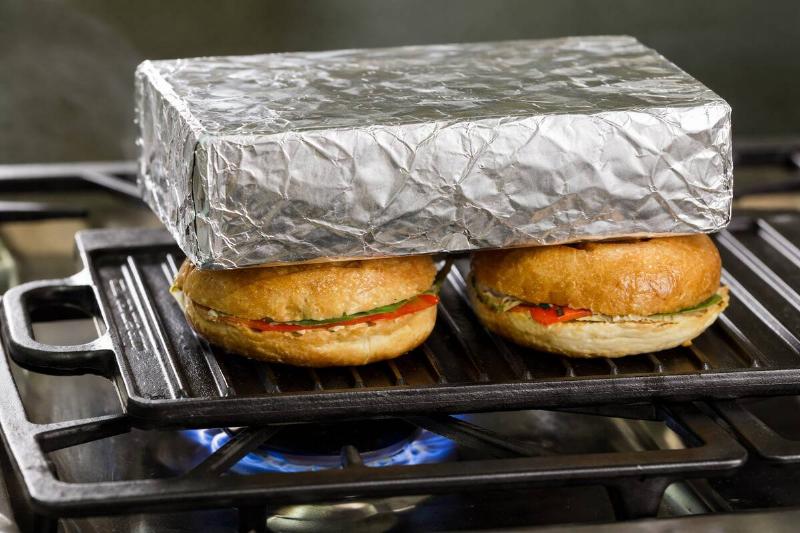 Ai rendering of a brick, wrapped in aluminum foil, placed atop two sandwiches being cooked on a griddle