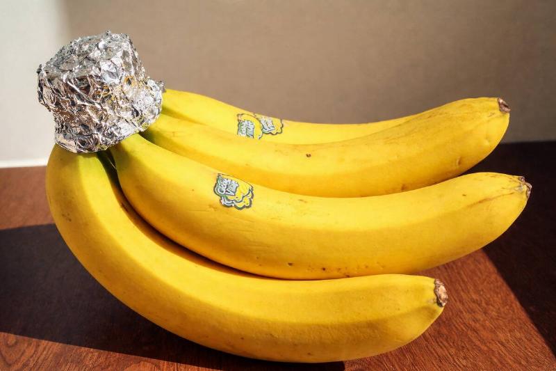 AI rendering of a bunch of bananas, placed on a wooden surface, with aluminum foil wrapped around their stems