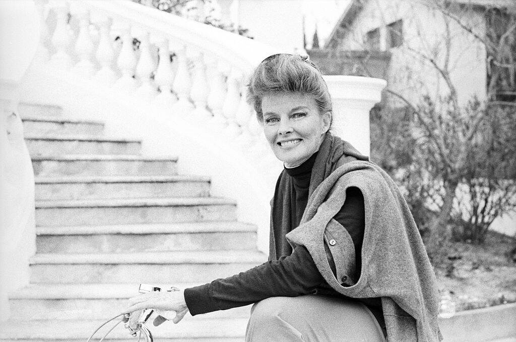 Katharine Hepburn riding a bicycle past an outdoor staircase