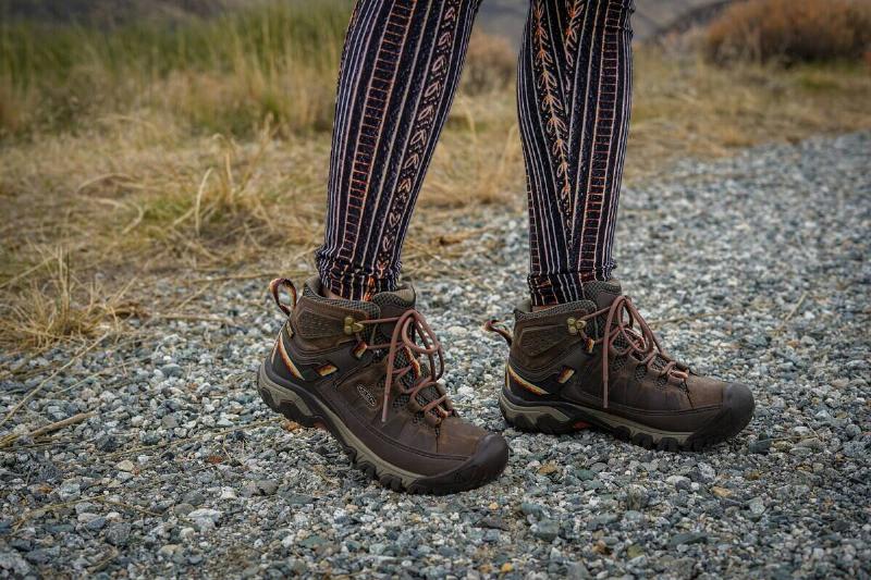 Close-up of the bottom half of a person standing on a rocky path outdoors. They are wearing patterned leggings and hiking shoes